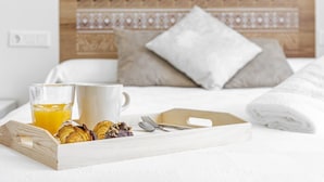 Ein ordentlich bezogenes Bett mit einem gemusterten Kopfteil, ein Tablett mit Croissants und einem Glas Orangensaft sowie eine weiße Tasse.