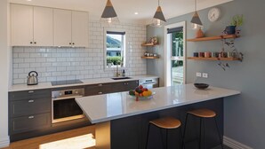 A modern kitchen with white cabinets, a large island with stools, pendant lighting, and a view of greenery outside.
