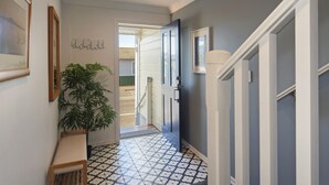 A hallway with patterned floor tiles, a potted plant, and framed pictures on the walls.