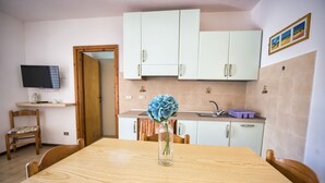 A compact kitchen with white cabinets, a wooden dining table, and a vase with flowers. - ALLOGGI DEL MIRTO - BILLY DEL MIRTO (Capoliveri)