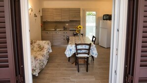 A compact kitchen with wooden cabinets, a dining table with chairs, and a refrigerator. - ALLOGGI DEL MIRTO - TRILLY DEL MIRTO (Capoliveri)