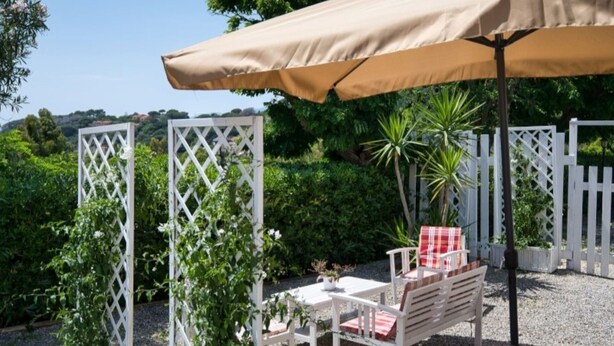 A patio with a white lattice structure, a table with chairs, and a beige umbrella. - ALLOGGI DEL MIRTO - TRILLY DEL MIRTO (Capoliveri)