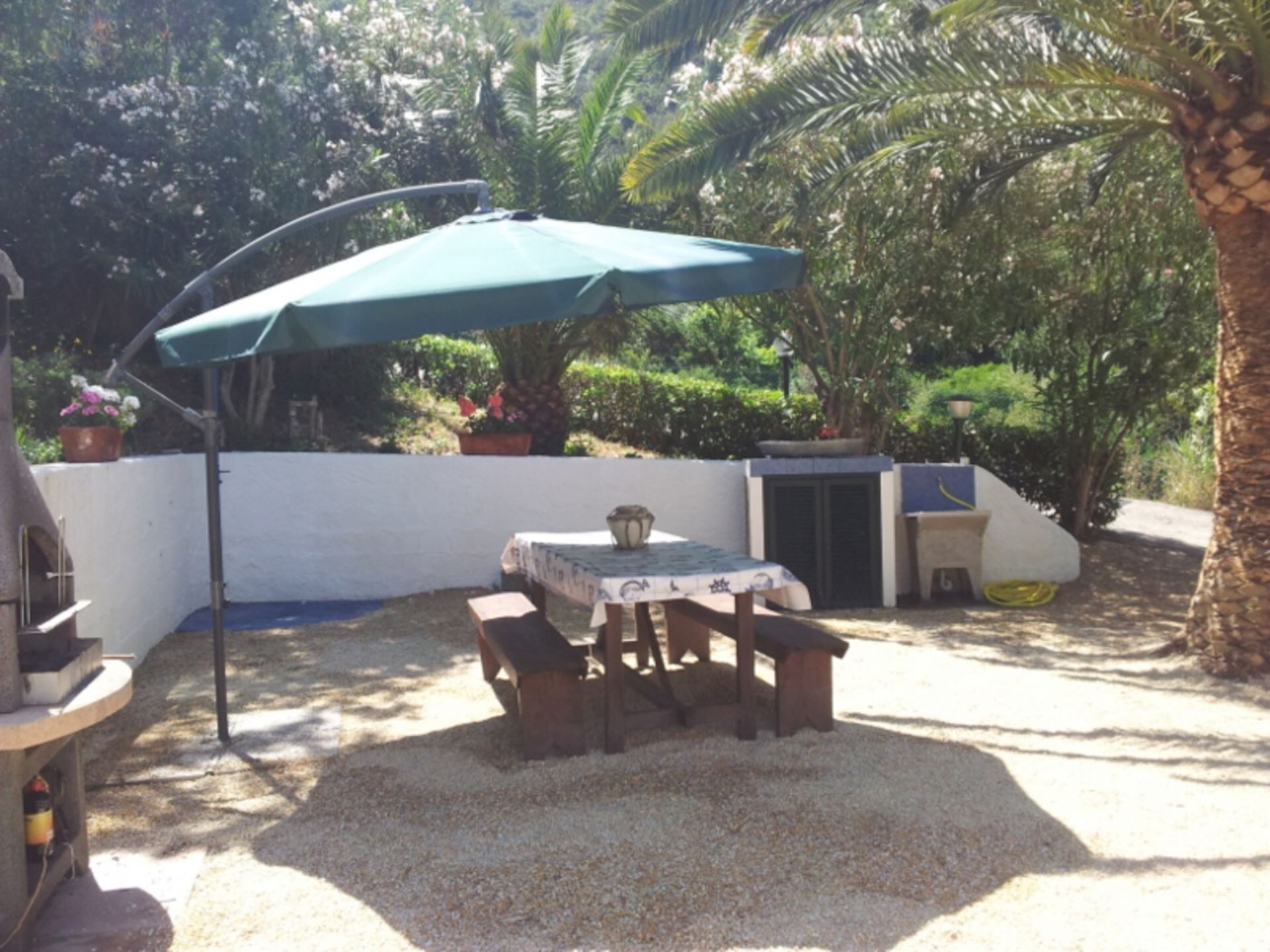 An outdoor patio with a table and chairs, a green umbrella, and a barbecue grill.