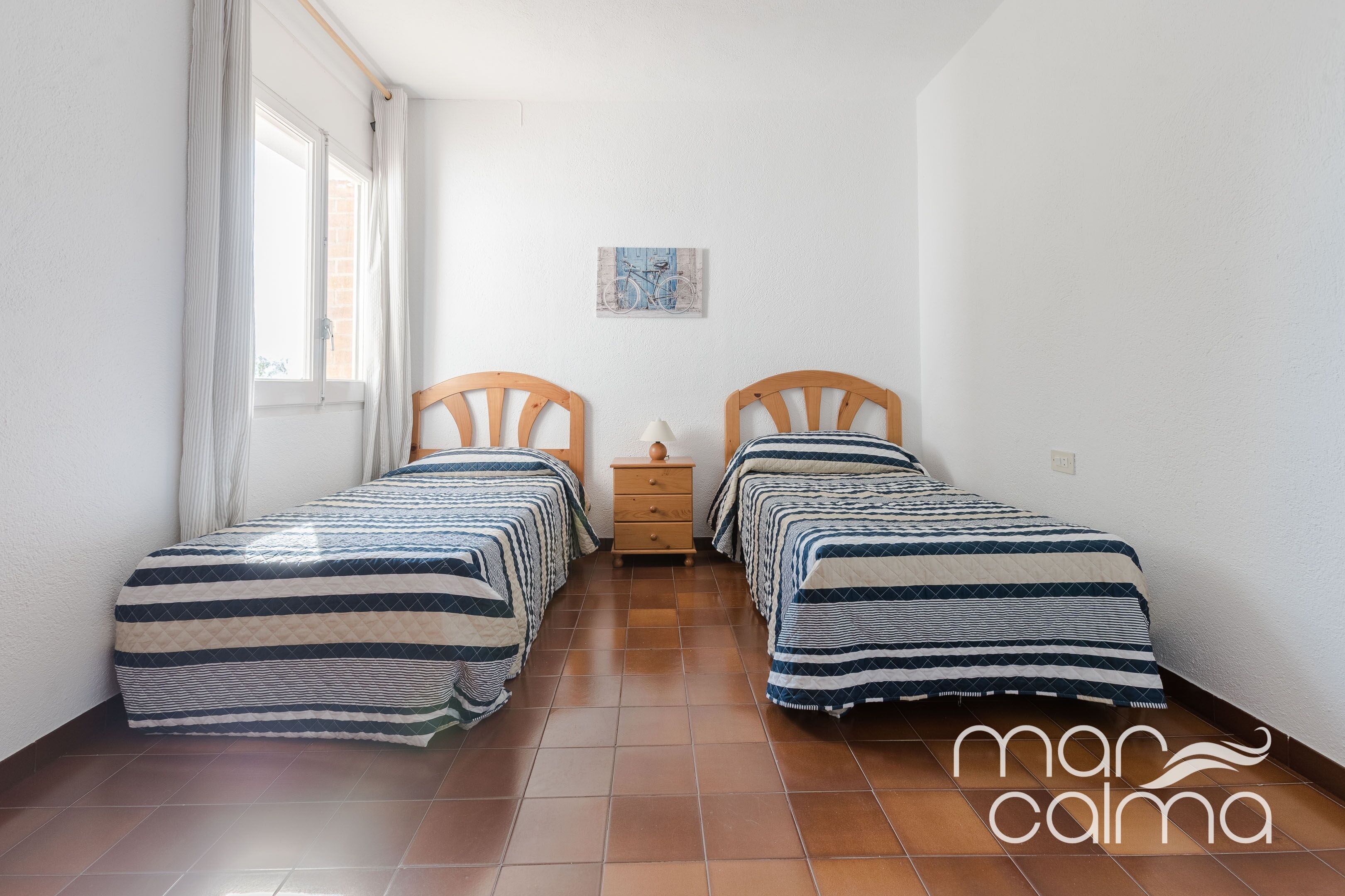 A small, clean room with two beds, a nightstand, and a window with curtains.