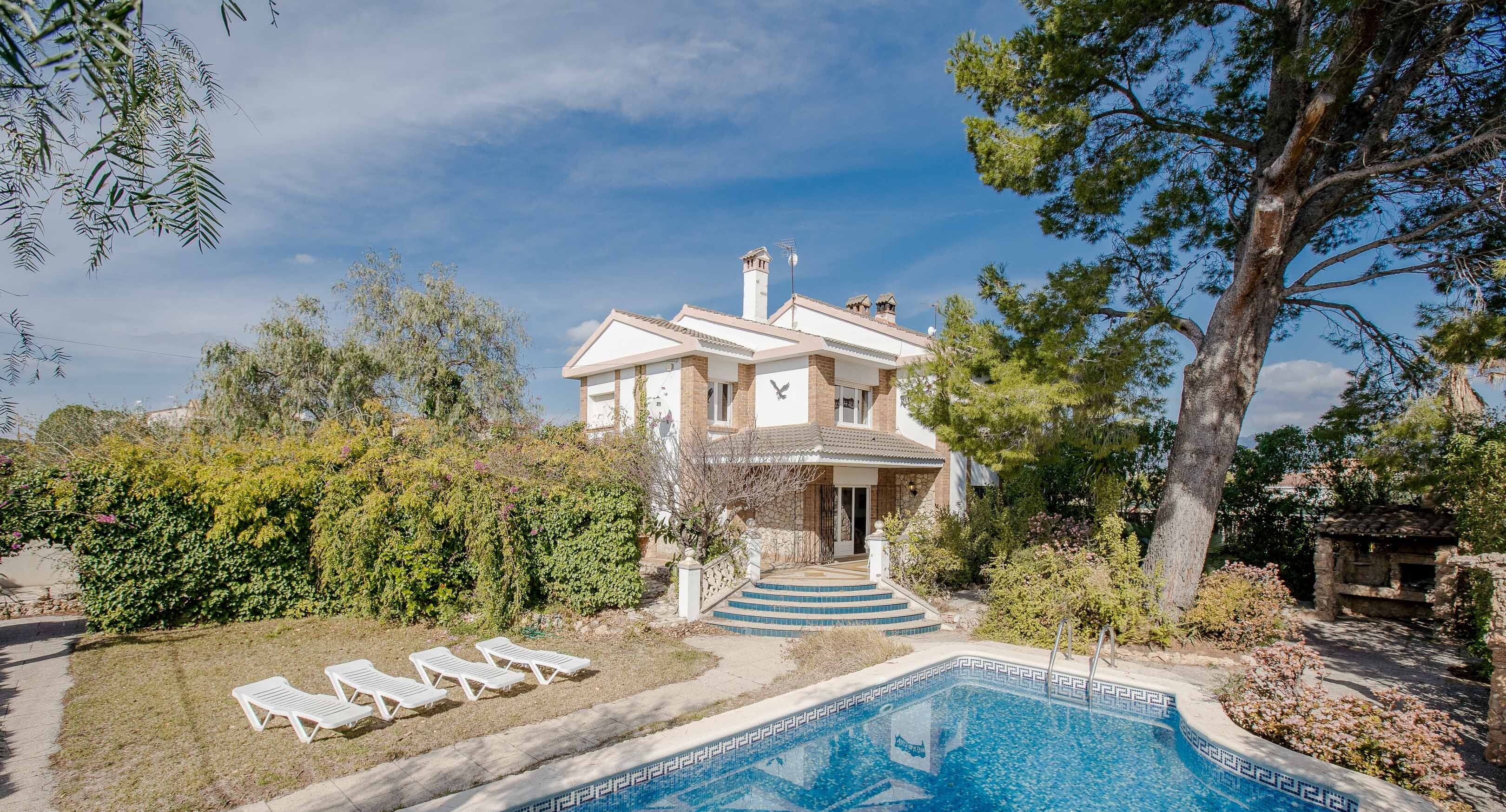 Una casa con piscina, rodeada de follaje y un cielo despejado.