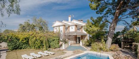 Una casa con piscina, rodeada de follaje y un cielo despejado.