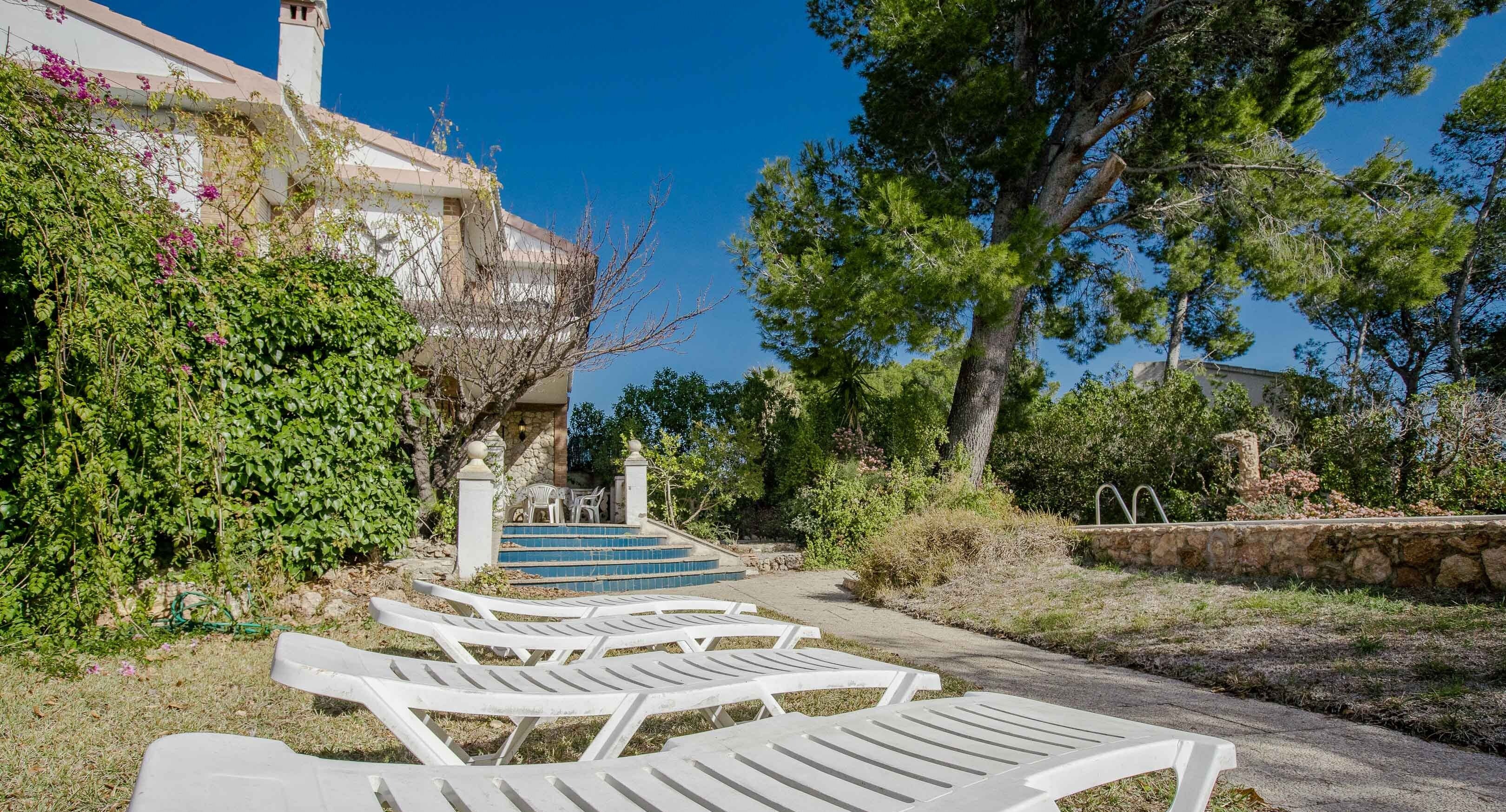 Outdoor lounge chairs, a stone wall, and a building with a staircase.