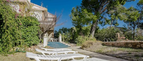 Outdoor lounge chairs, a stone wall, and a building with a staircase.