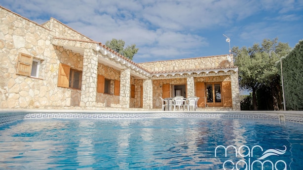 Ein Gebäude aus Stein mit einem Pool, ausgestattet mit einer Terrasse, auf der Stühle und ein Tisch stehen.