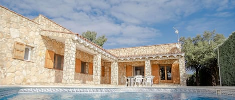 A stone building with a pool, featuring a patio with chairs and a table.