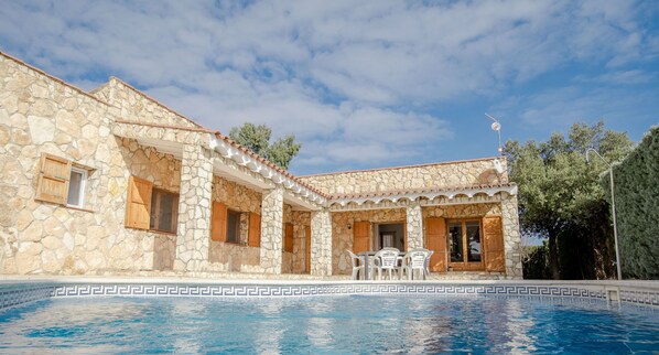 A stone building with a pool, featuring a patio with chairs and a table.