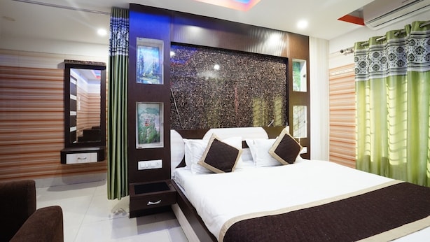 A modern bedroom with a large bed, a dresser, a mirror, and a wall-mounted TV. - Tirupati Lodge Private Limited (Jalpaiguri)