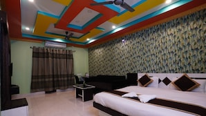 A hotel room with a bed, a desk, a chair, a ceiling fan, and a patterned wall. - Tirupati Lodge Private Limited (Jalpaiguri)
