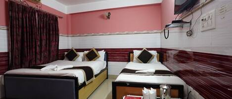 A hotel room with two beds, a small table with a pitcher and napkins, and a TV mounted on the wall.