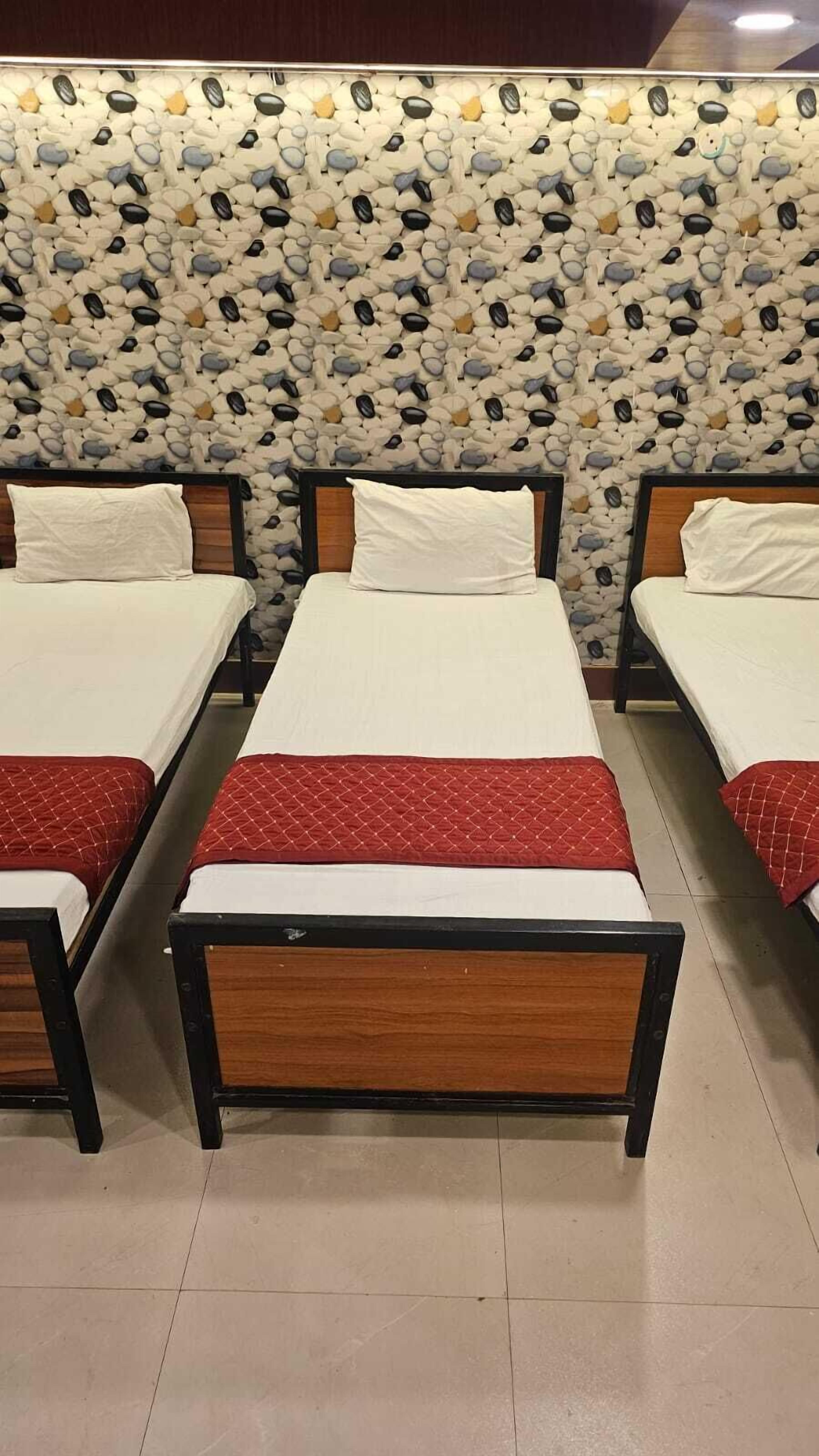 A row of four single beds with wooden frames and white bedding, arranged in a row with a pebble-patterned wall behind them.