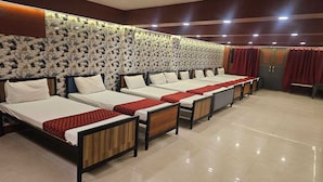 A hotel room with multiple beds arranged in a row, a decorative wall with a pebble pattern, and a red curtain. - Tirupati Lodge Private Limited (Jalpaiguri)