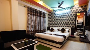 A hotel room with a bed, a sofa, a small table, a ceiling fan, and a patterned wall. - Tirupati Lodge Private Limited (Jalpaiguri)