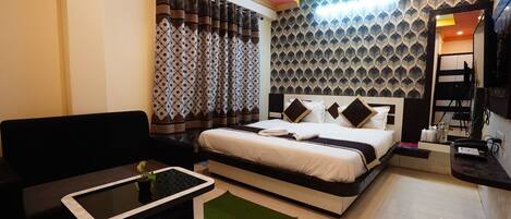 A hotel room with a bed, a sofa, a small table, a ceiling fan, and a patterned wall.