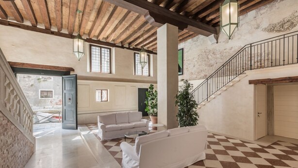 Un'ampia zona giorno con pavimento a scacchi, divani bianchi e una scala con ringhiera in metallo.