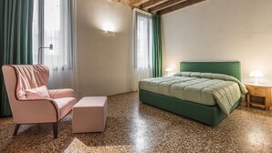 Una camera da letto con un letto verde, una sedia rosa, un tavolino e una lampada.