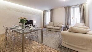 Un soggiorno moderno con un tavolo da pranzo in vetro, sedie trasparenti, un divano color beige e una televisione.