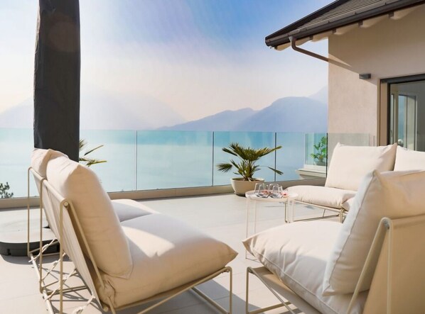 Ein Balkon mit zwei beigen Liegestühlen, einem kleinen Tisch mit Getränken und einem Blumentopf.