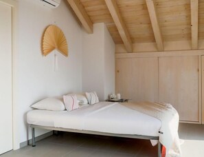 Ein Schlafzimmer mit einem Bett, Kissen, einem Nachttisch und einem Wandventilator.