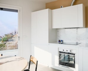 Uma cozinha moderna com armários brancos, forno embutido e vista através de uma grande janela.