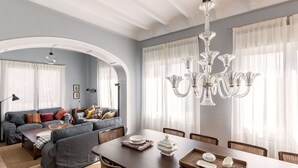 Ein Essbereich mit einem langen Tisch, Stühlen und einer Chandelier. An der angrenzenden Wohnbereich befindet sich eine Couch mit Kissen.