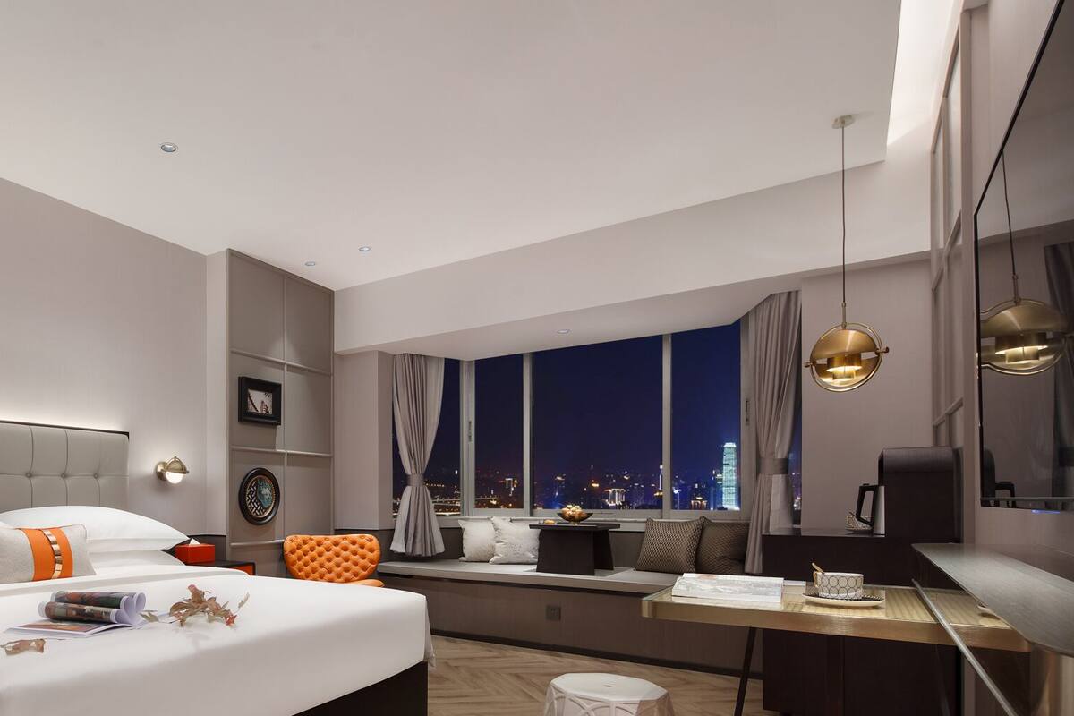 Une chambre d’hôtel moderne avec un grand lit, un bureau et une vue sur la ville la nuit.