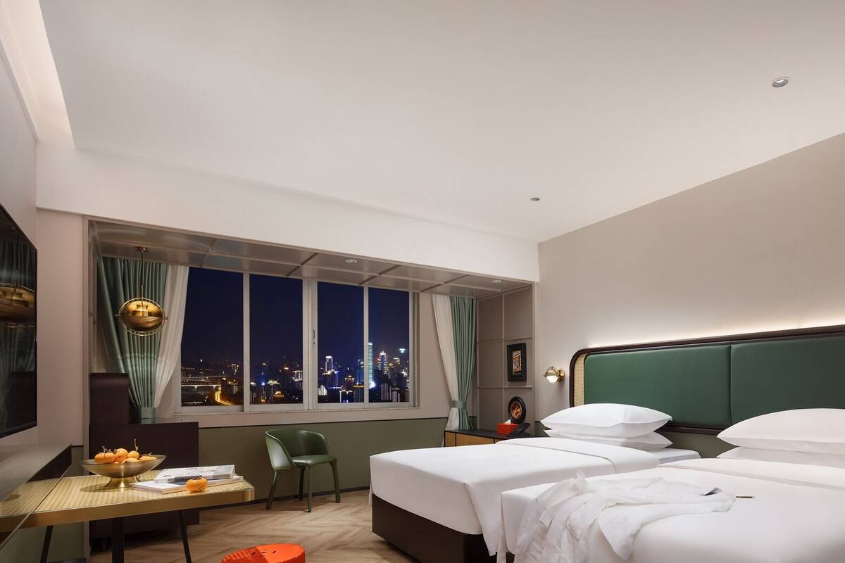 Une chambre d’hôtel avec vue sur la ville, deux lits, un bureau avec une chaise et une télévision.