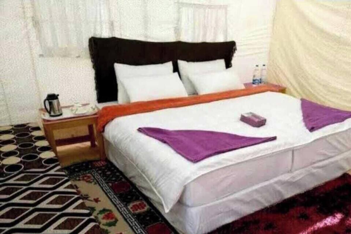 A bed with white bedding, a wooden nightstand, a patterned rug, and a red carpet.