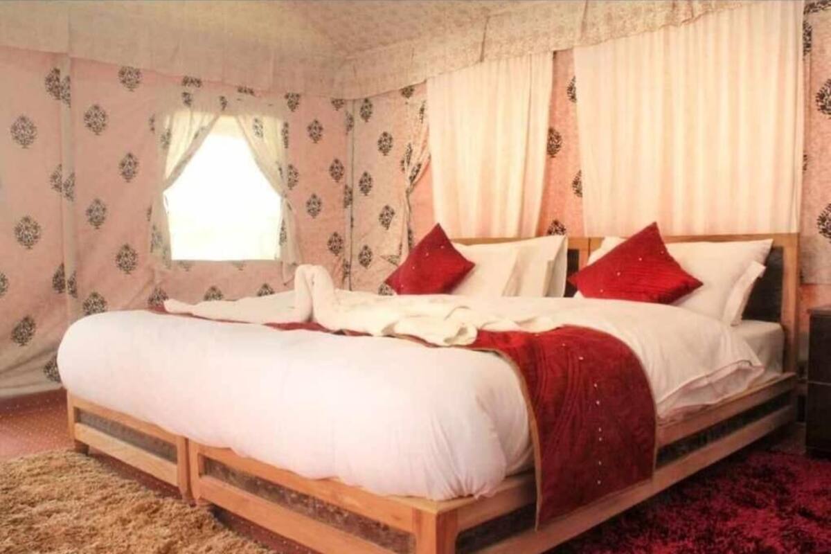 A bedroom with a wooden bed, white bedding, red pillows, and patterned curtains.