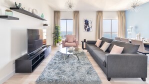 Een moderne woonkamer met een flatscreen televisie, een grijze bank en een ronde glazen salontafel.