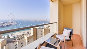 Een balkon met een glazen tafel, twee stoelen en uitzicht op een strand, een reuzenrad en gebouwen aan de overkant van het water.