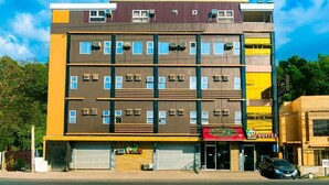 A multi-story hotel with a modern design, featuring balconies, air conditioning units, and a variety of ground-level shops. - FB Budgetel Suites (Cagayan de Oro)