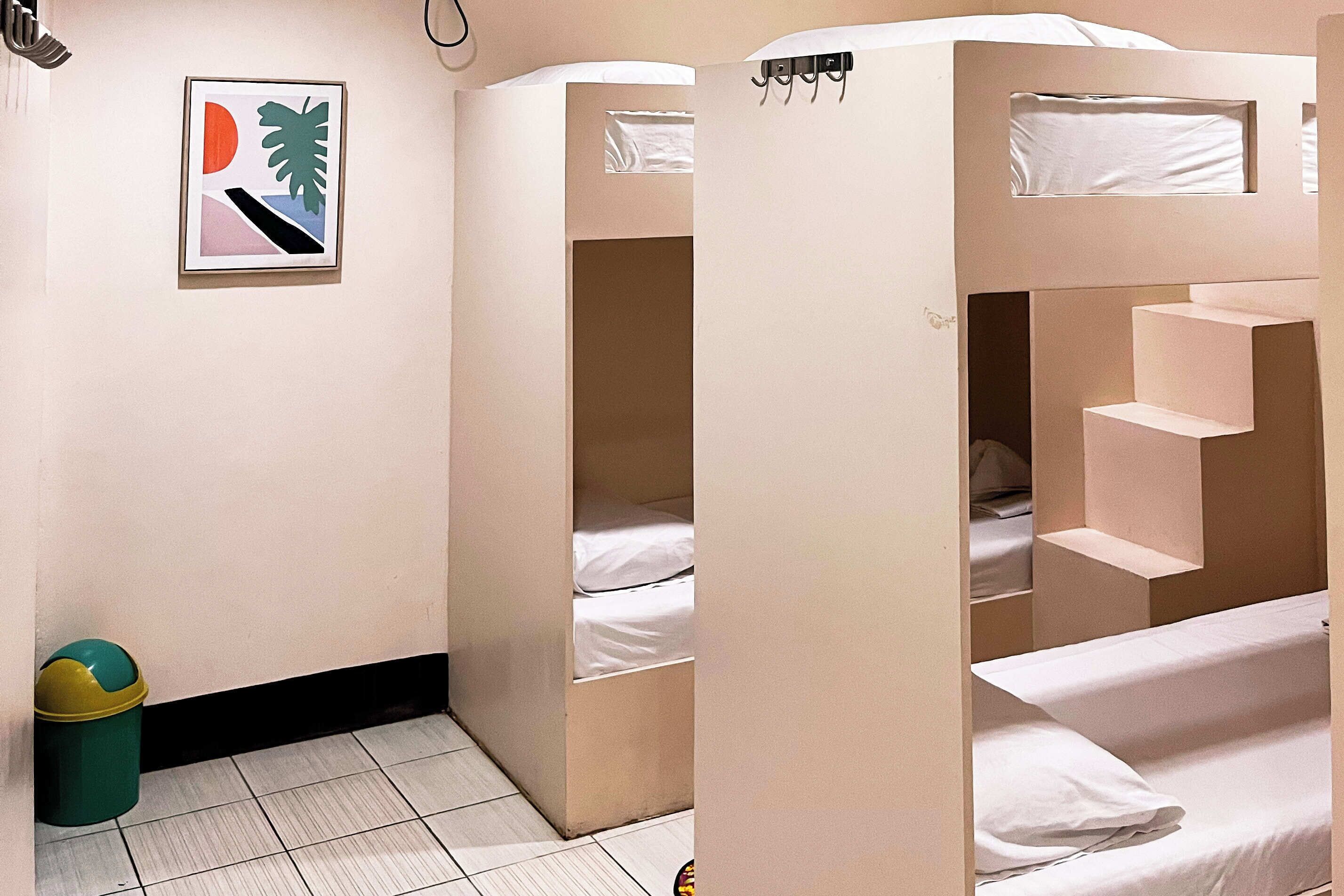 A room with bunk beds, a trash bin, and a framed picture on the wall.