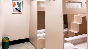 A room with bunk beds, a trash bin, and a framed picture on the wall.