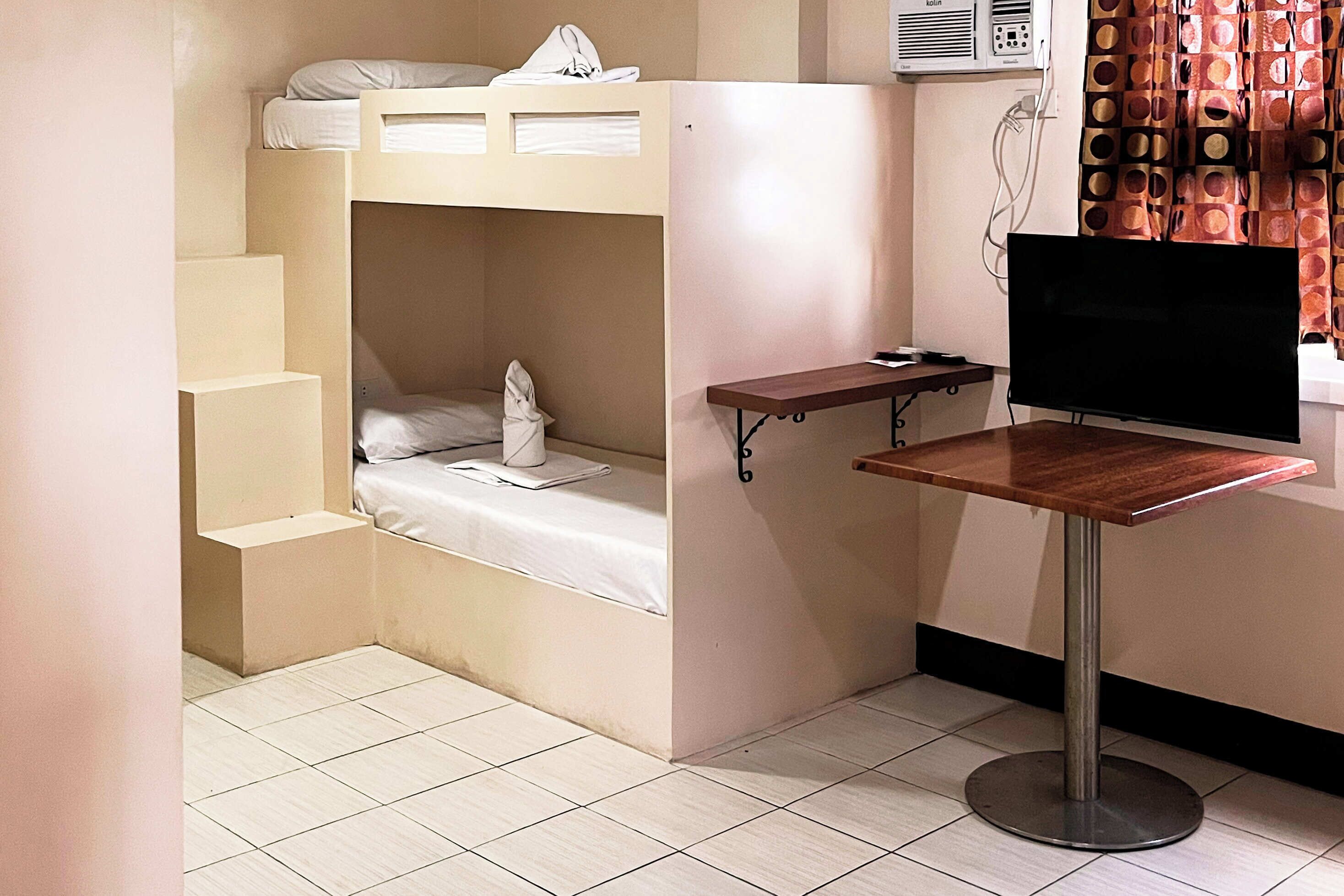 Habitación pequeña con una cama litera, una mesita y un televisor.