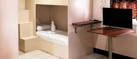 Habitación pequeña con una cama litera, una mesita y un televisor.