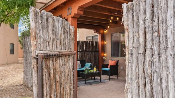 A patio area with rustic wooden fencing, outdoor seating with cushions, and string lights.