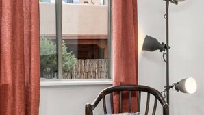 A room with a window, a chair with a patterned cushion, a floor lamp, and a rug.