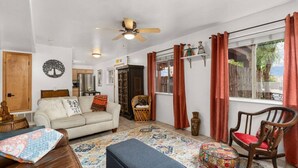 A cozy living room with a sofa, a rocking chair, a patterned rug, and a ceiling fan.