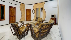 A spacious living area with a round coffee table, wicker chairs, and a television. - OYO Life 3956 Hotel Palem 2 Syariah (Malang)