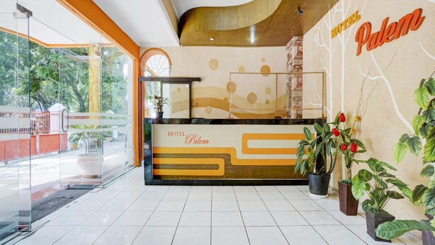 A hotel reception area with a modern design, including a reception desk, potted plants, and a view of the outdoors. - OYO Life 3956 Hotel Palem 2 Syariah (Malang)