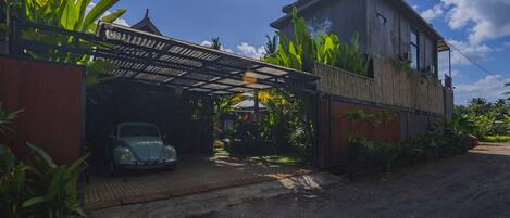 A house with a car parked under a covered area, surrounded by greenery.