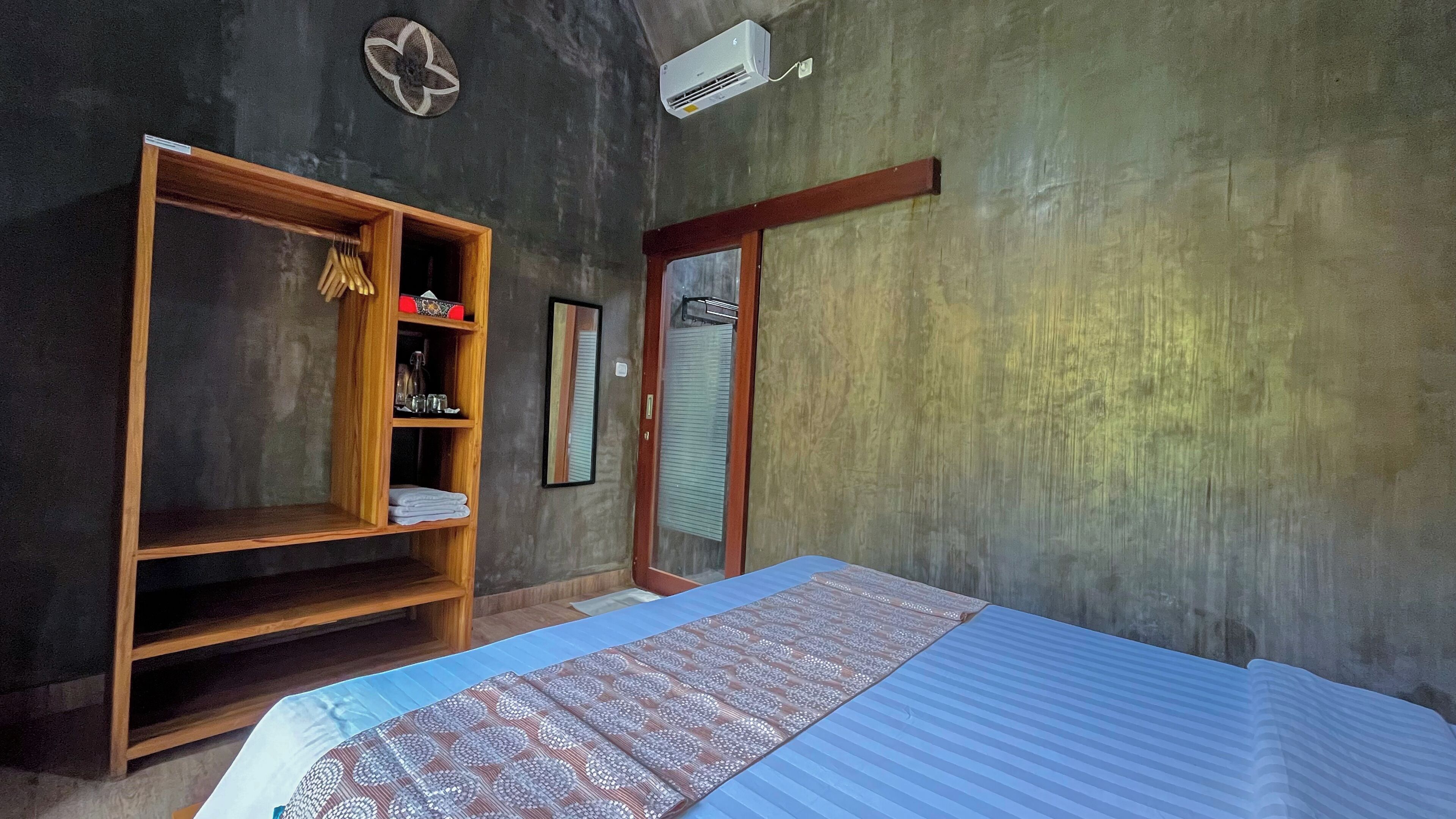 Una habitación con una cama, un armario de madera, un espejo y un equipo de aire acondicionado.