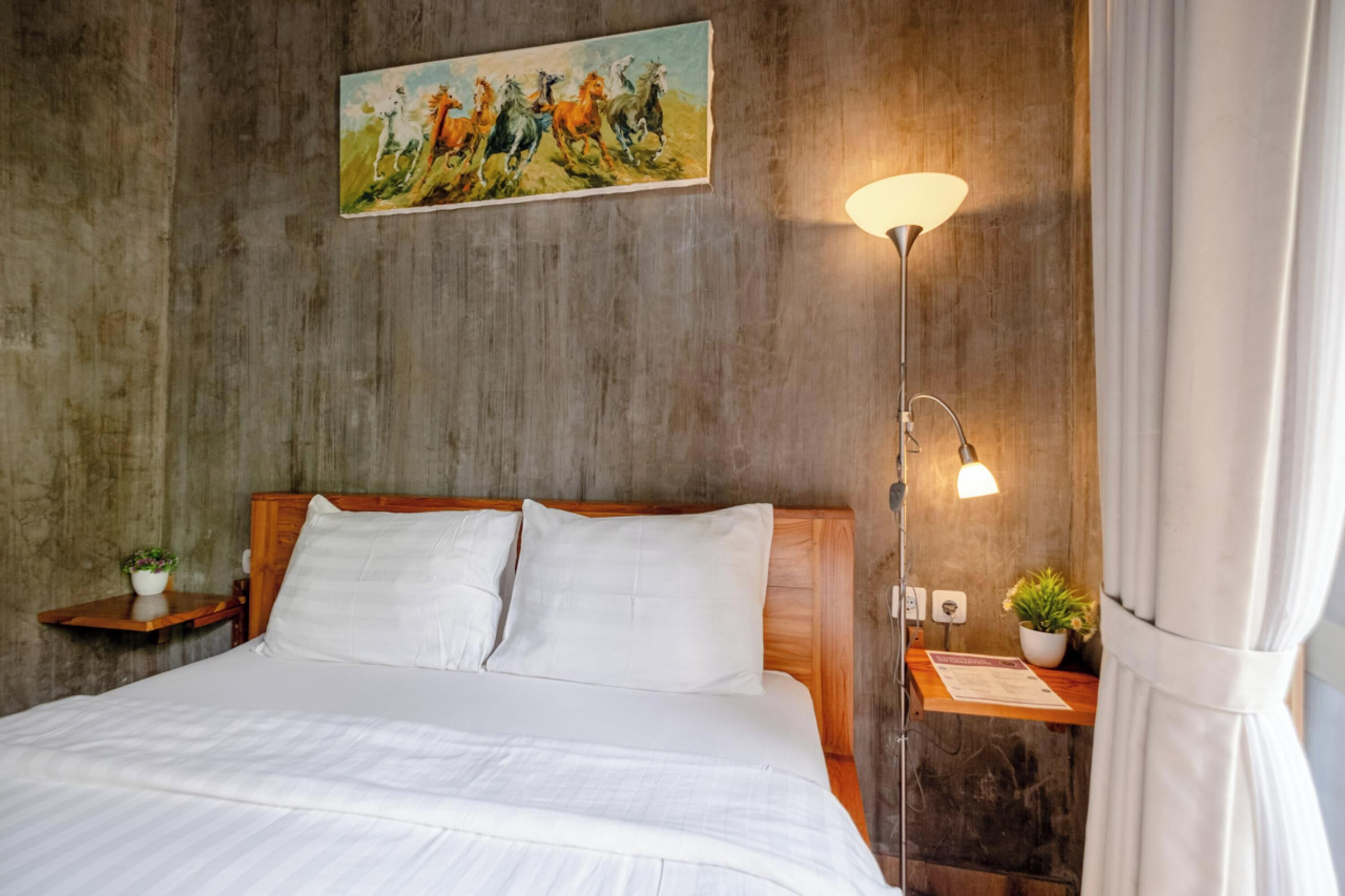 A neatly made bed with white linens, a wooden headboard, and a painting of horses on the wall.