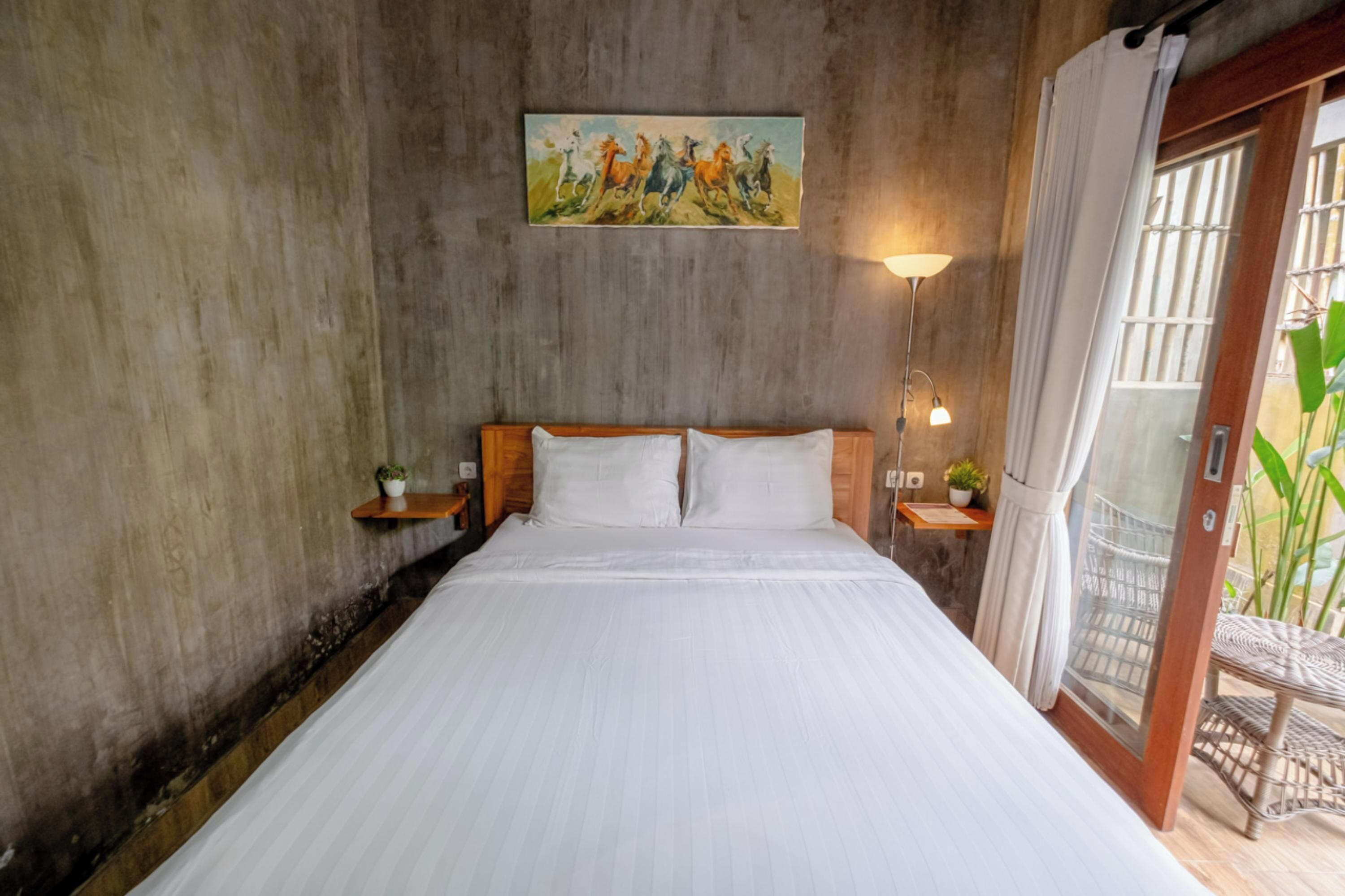 A bedroom with a wooden headboard, white bedding, a painting above the bed, bedside tables with plants, and a view through a glass door.