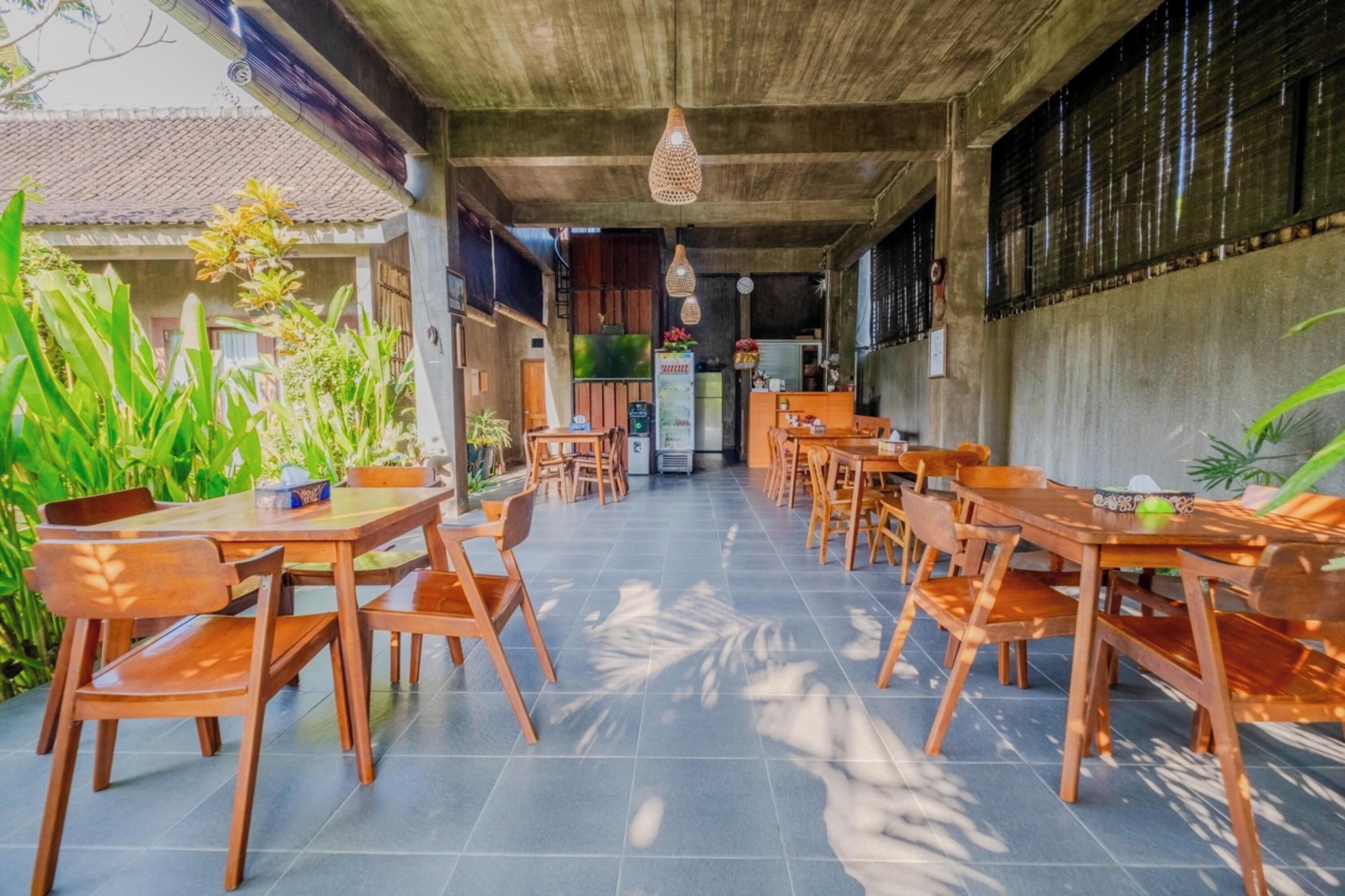 An outdoor dining area with wooden tables and chairs, surrounded by greenery.